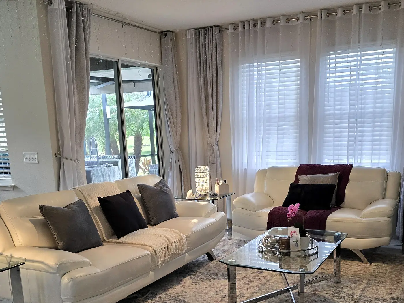 Living room with white leather sofas, a glass coffee table and sliding doors to a screened lanai